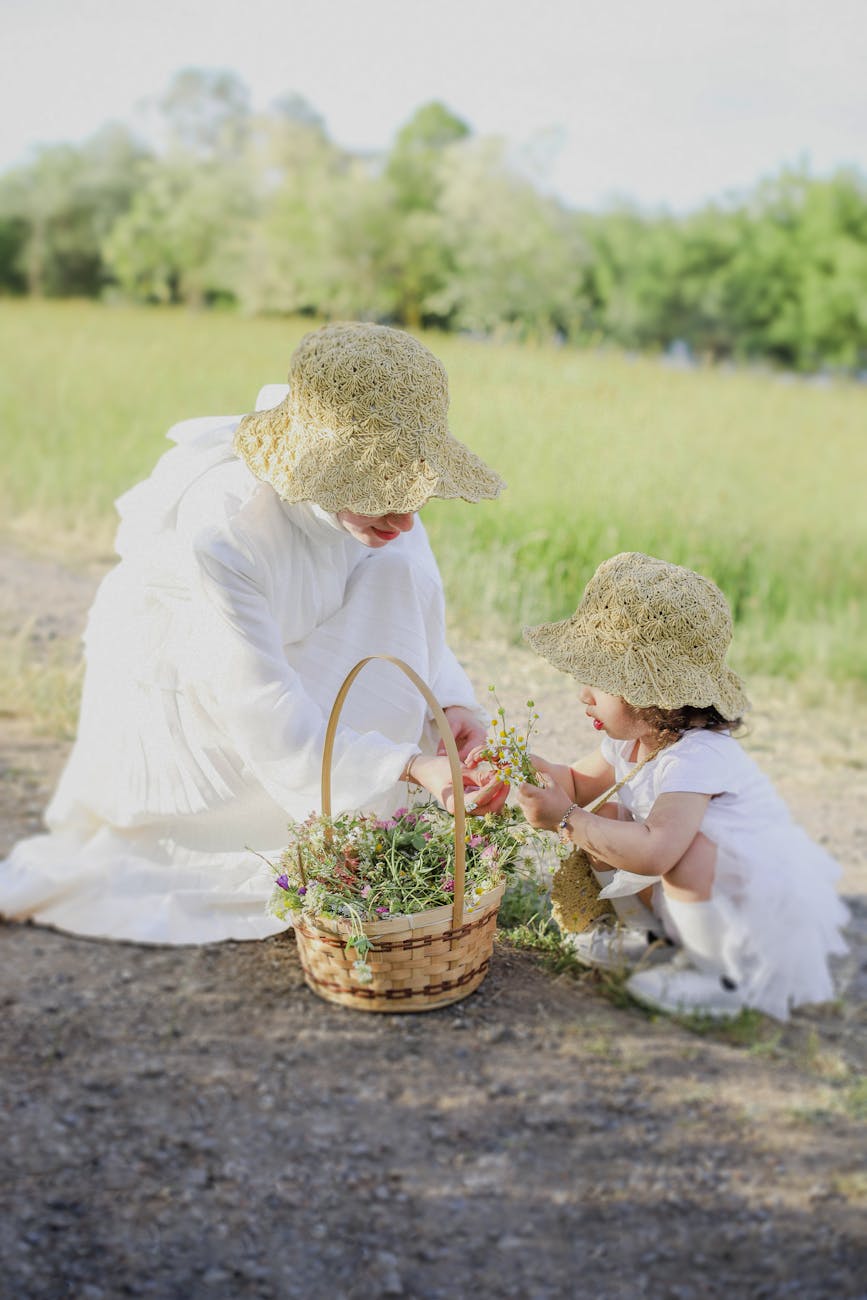 mother and daughter in white dresses and hats picking flowers on a meadow