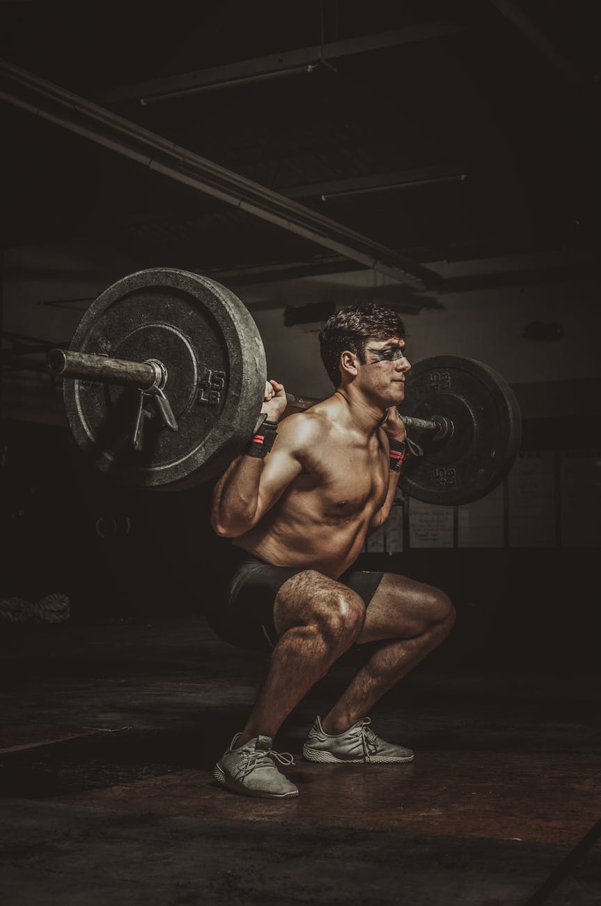 a topless man in black shorts doing squats with a barbell